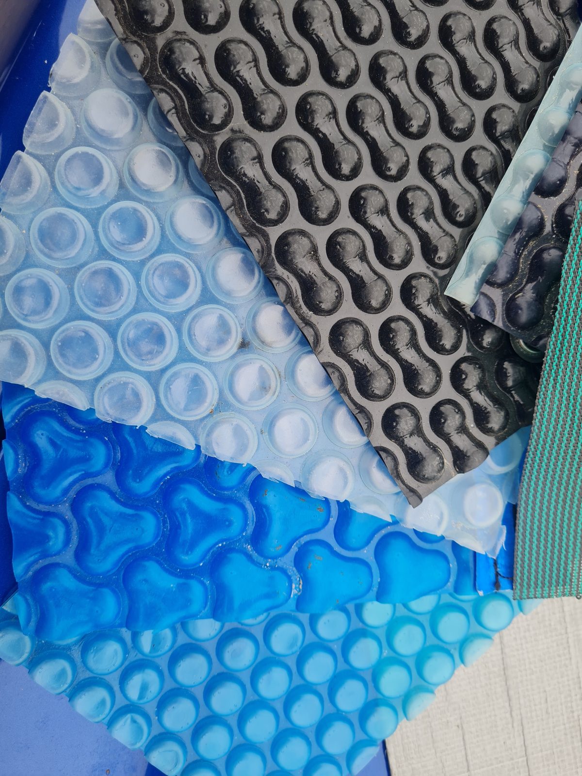 Samples of pool cover material in clear, blue and black bubble patterns