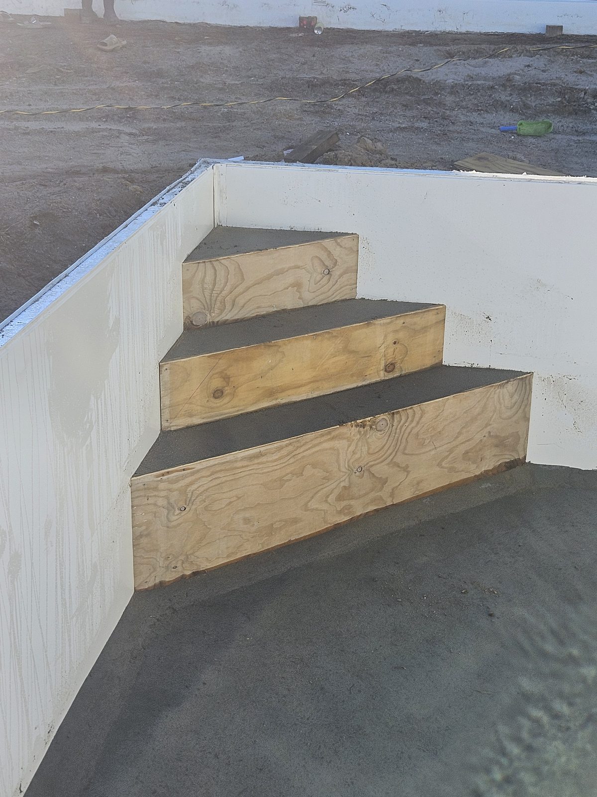Plywood formwork for a set of entry steps in the corner of a pool under construction