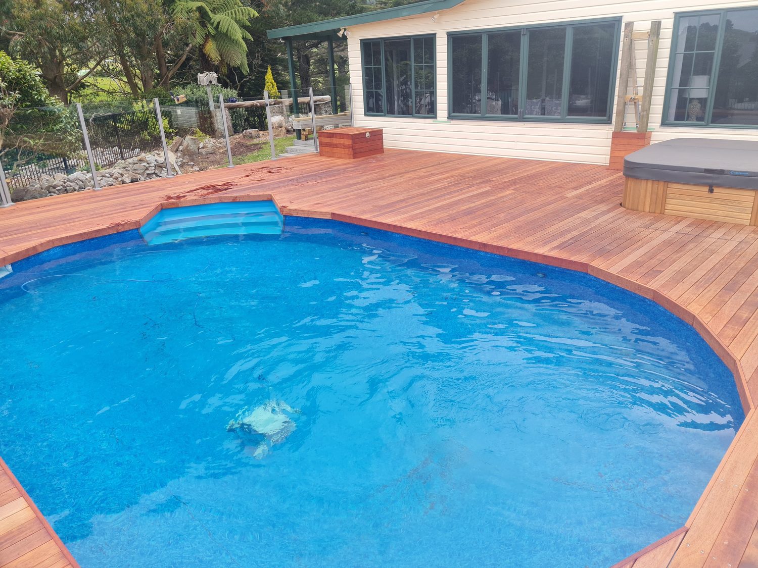 A pool set into a hardwood deck beside a house, with a spa on the deck