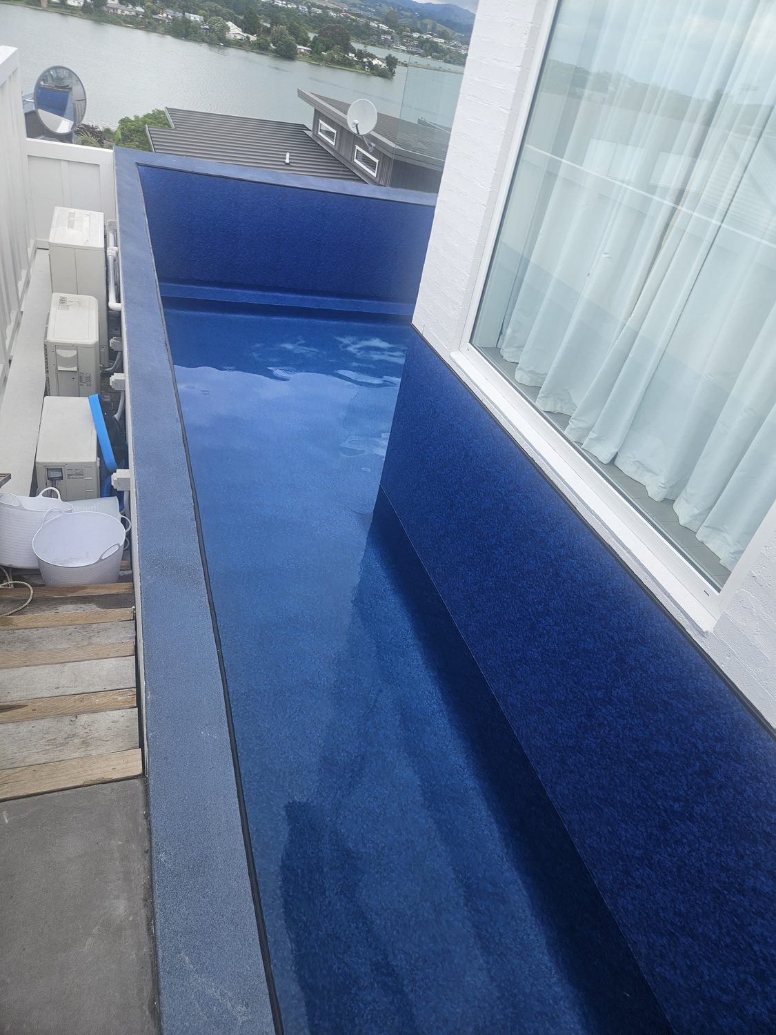 A narrow pool with a dark blue liner running along the side of a house