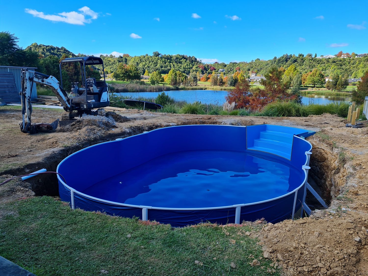 A newly installed blue liner pool with a digger and a lake in the background
