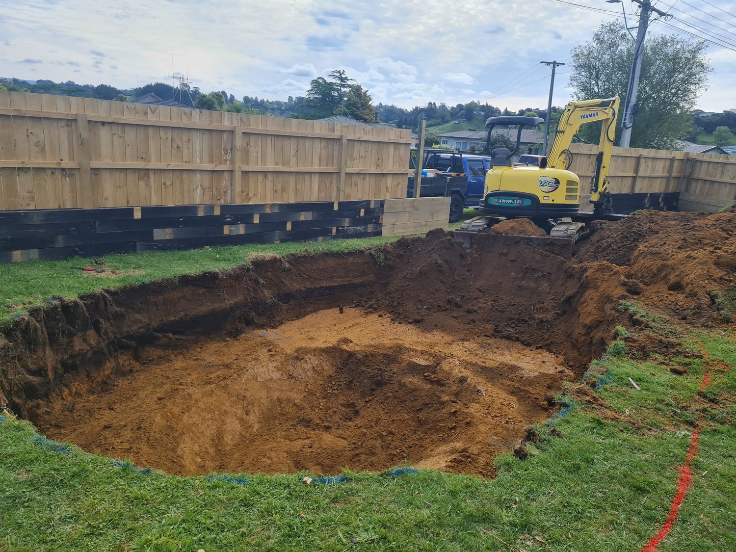 A digger beside a pool excavation in a back yard