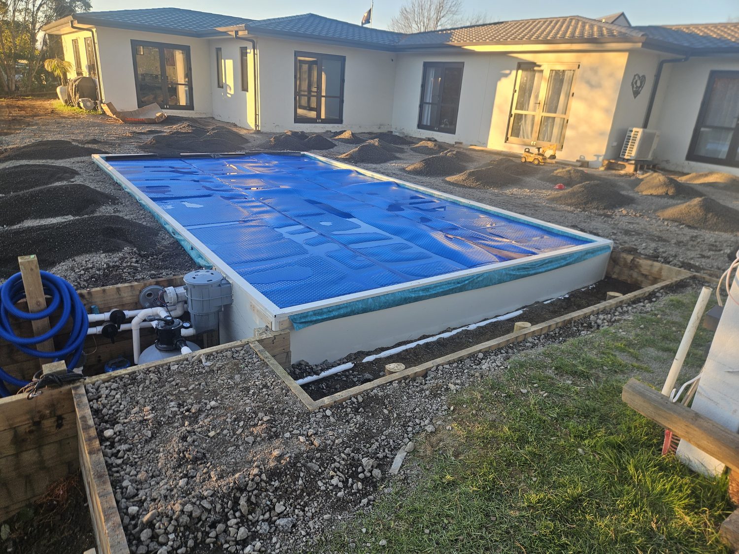 A rectangular pool under a blue solar cover, with the surrounding deck still being built