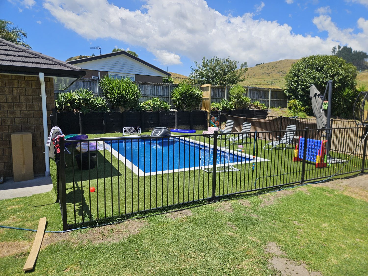 A rectangular pool on a fenced lawn with pool toys on the grass
