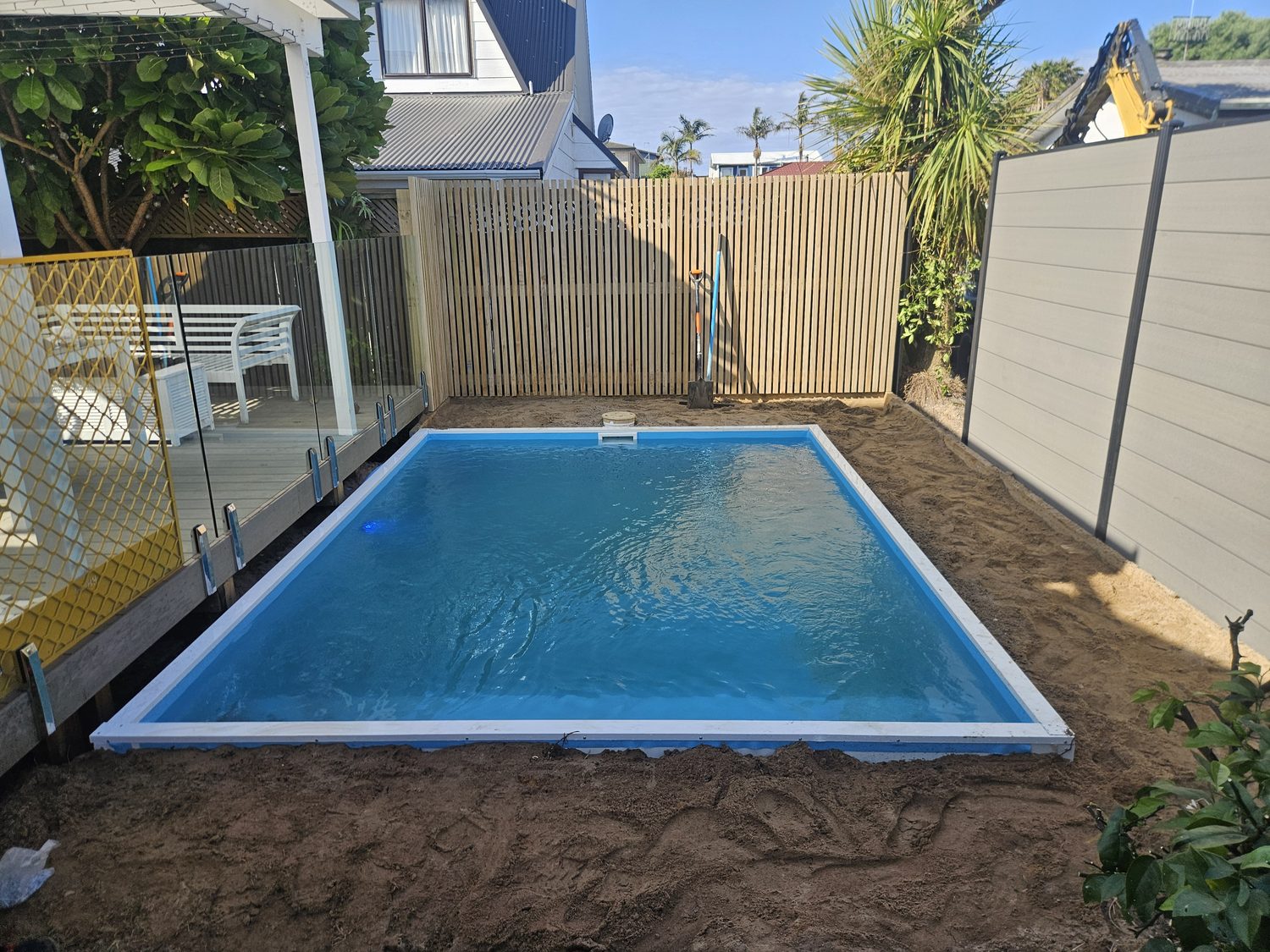 A small rectangular pool behind a glass fence in a compact back yard