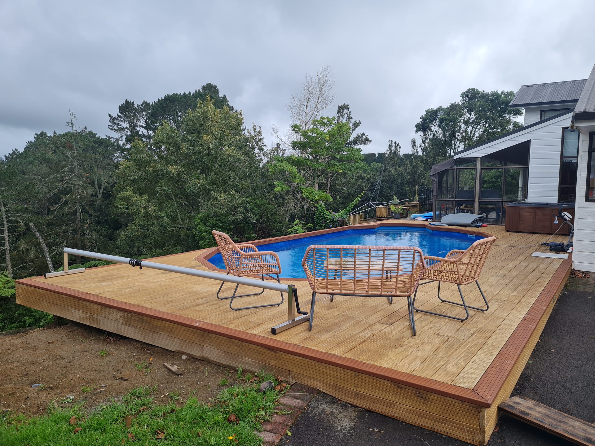 A pool set into a raised timber deck with outdoor chairs and a cover roller