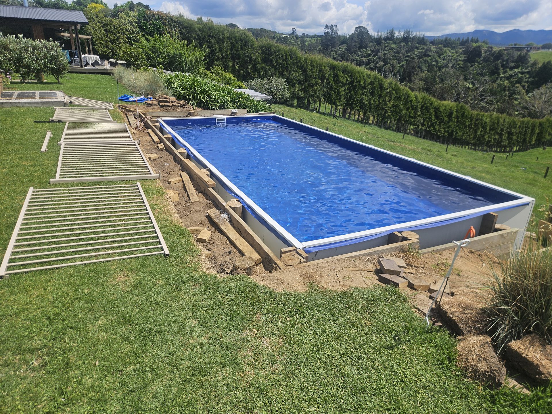 A long rectangular liner pool set into a lawn, with hedges and bush-covered hills behind