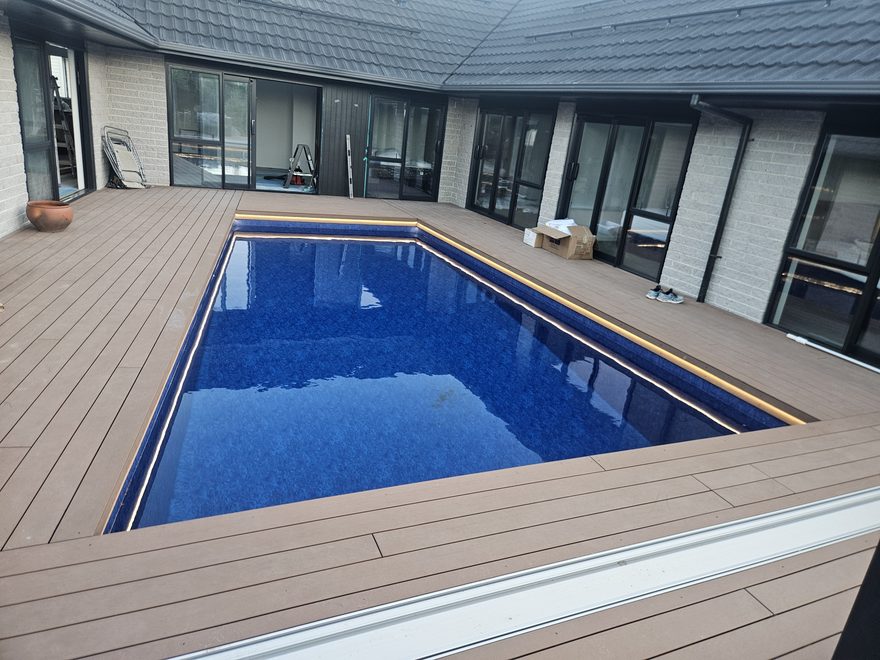 A rectangular in-ground pool set into a timber deck beside a house